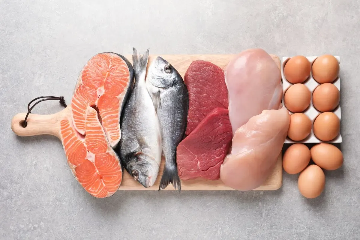 Salmon, whole fish, beef, chicken breast and eggs arranged on a wooden board